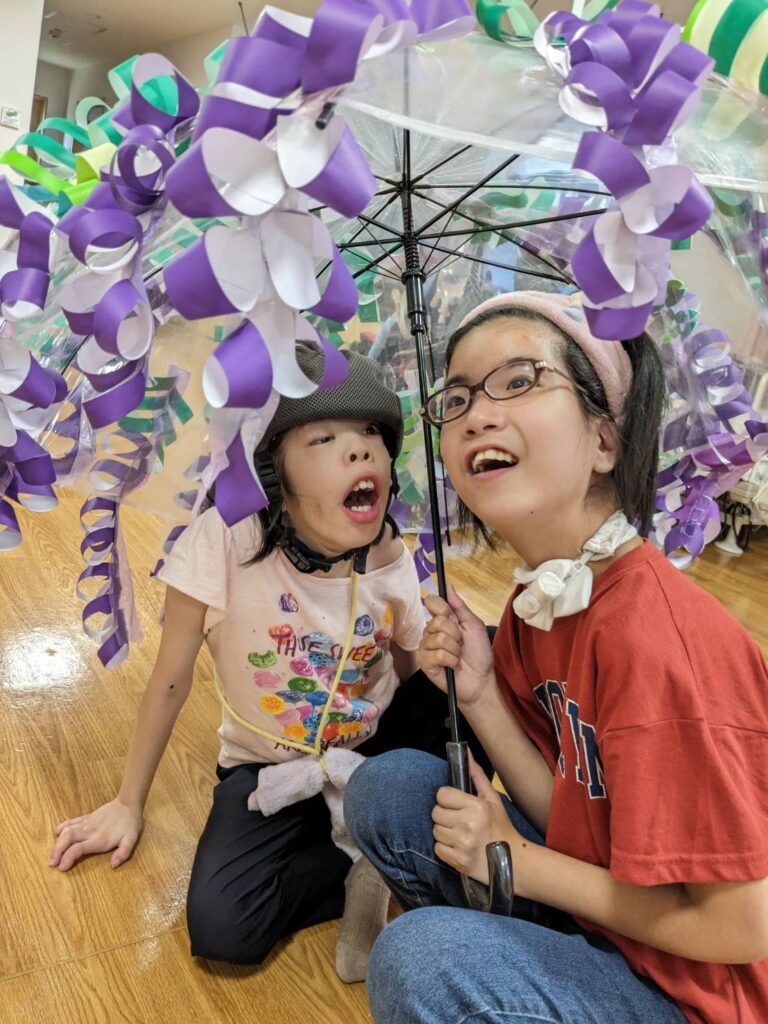 さん　藤の花の飾りのついた傘をさして笑顔の利用者様
