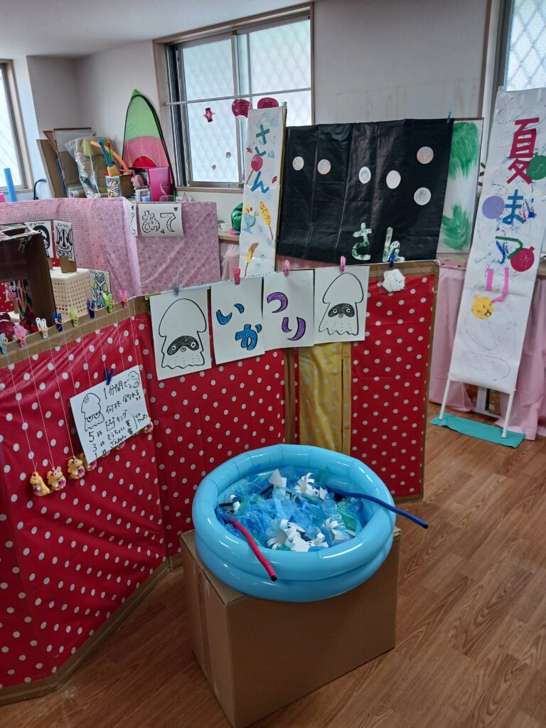 さん　フロアで夏祭りの飾りつけをして、イカ釣りなどの出店がある